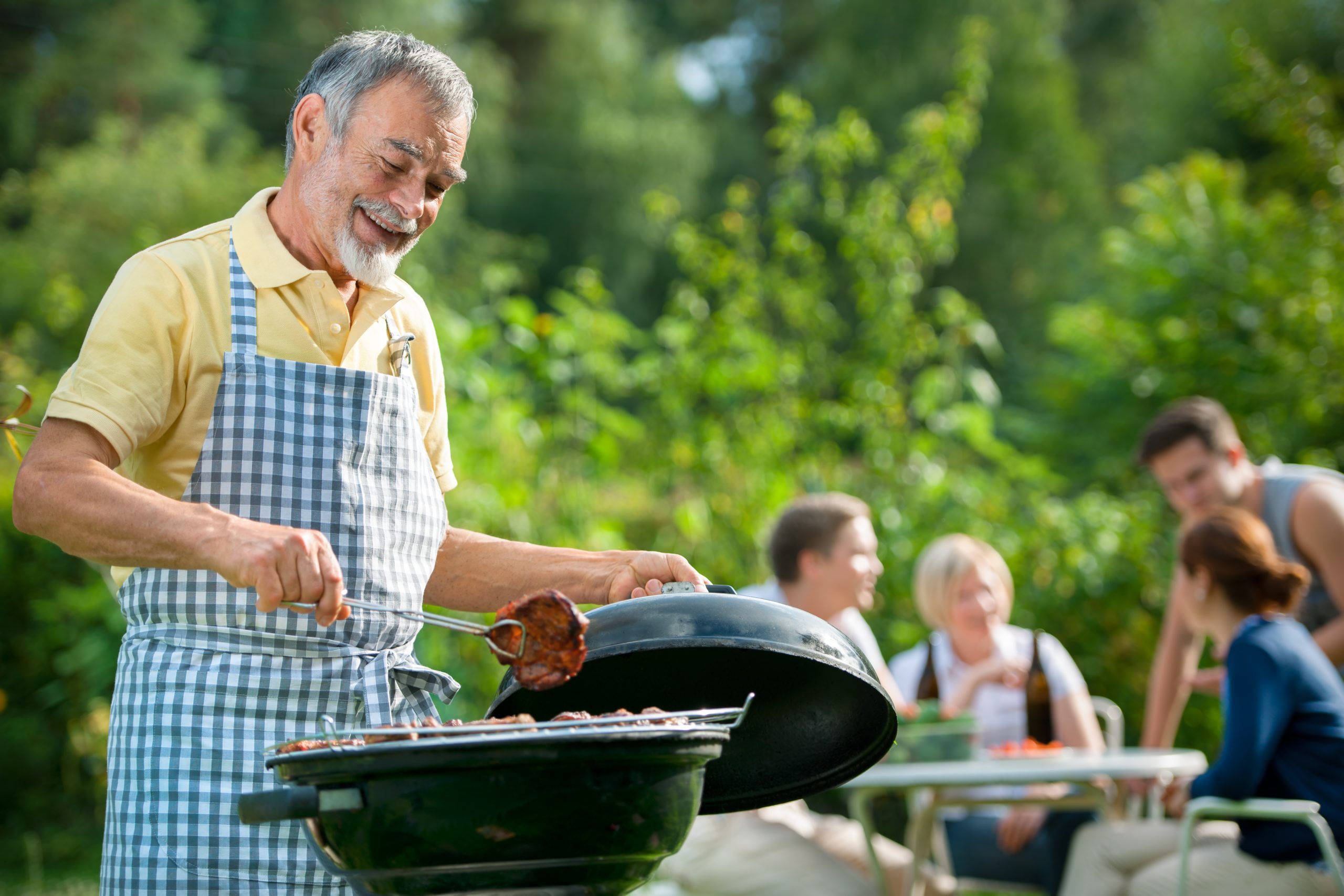 Older man barbecuing outside with family in background