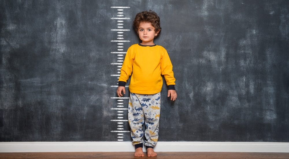 Funny,Smiling,Little,Child,With,Measures,Of,Growth,On,Blackboard