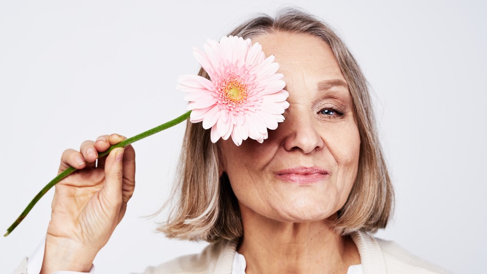 Cheerful,Elegant,Elderly,Woman,Holding,A,Flower,Near,The,Face