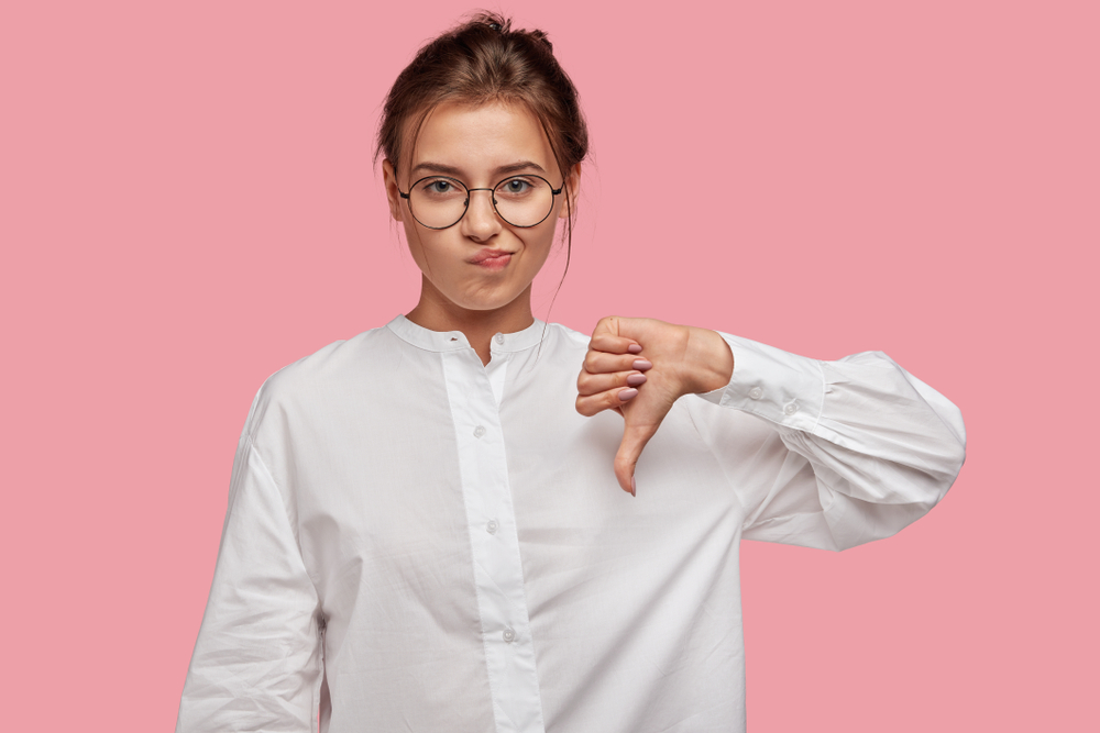 Discontent,European,Woman,Shows,Diapproval,Sign,,Keeps,Thumb,Down,,Expresses