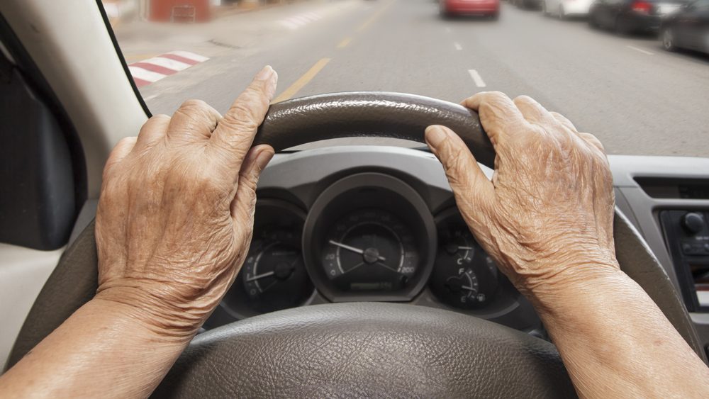 Senior,Woman,Driving,A,Car,On,Street,In,City.