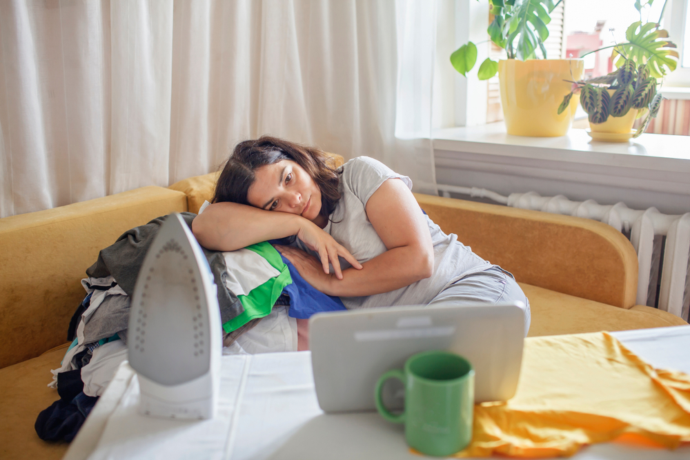 Tired,Middle,Aged,Woman,Watches,Video,On,Tablet,And,Ironing