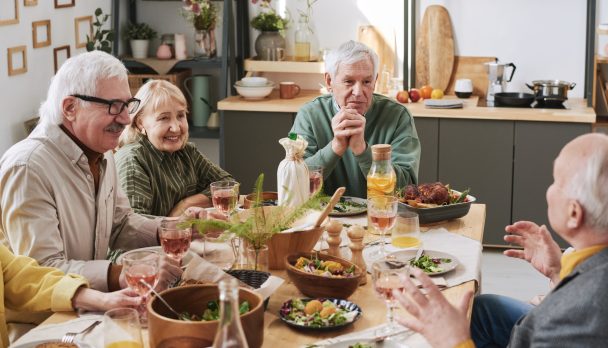 Senior people sitting at dining table and talking to each other during dinner at home