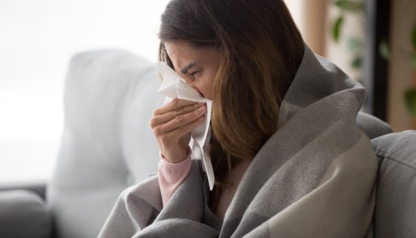 Ill,Upset,Young,Woman,Sitting,On,Sofa,Covered,With,Blanket