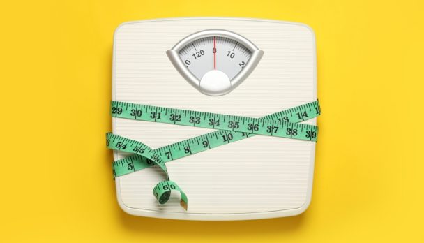 Weigh,Scales,Tied,With,Measuring,Tape,On,Yellow,Background,,Top