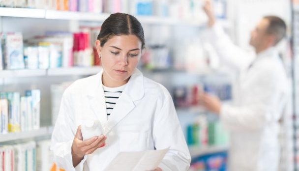 Young,Female,Pharmacist,In,Uniform,Looking,For,Prescription,Medicine,In